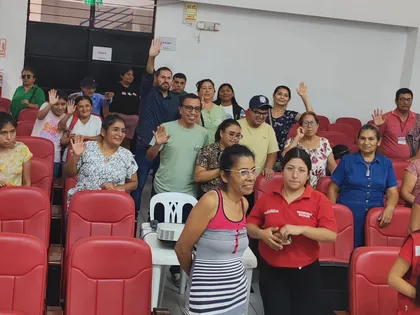 Comunidad reunida en un auditorio saludando a la cámara