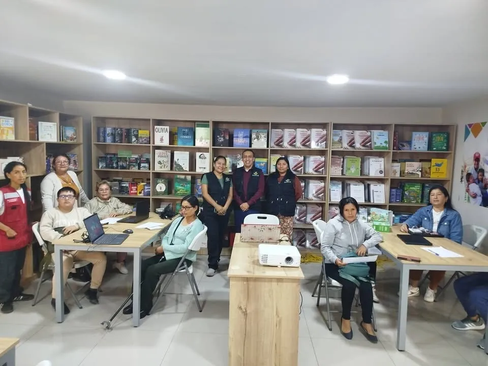 Voluntarios y participantes de pie en una sala con estanterías de libros durante una sesión de trabajo